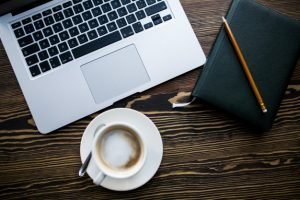 Ordenador, café, cuaderno y boligrafo.